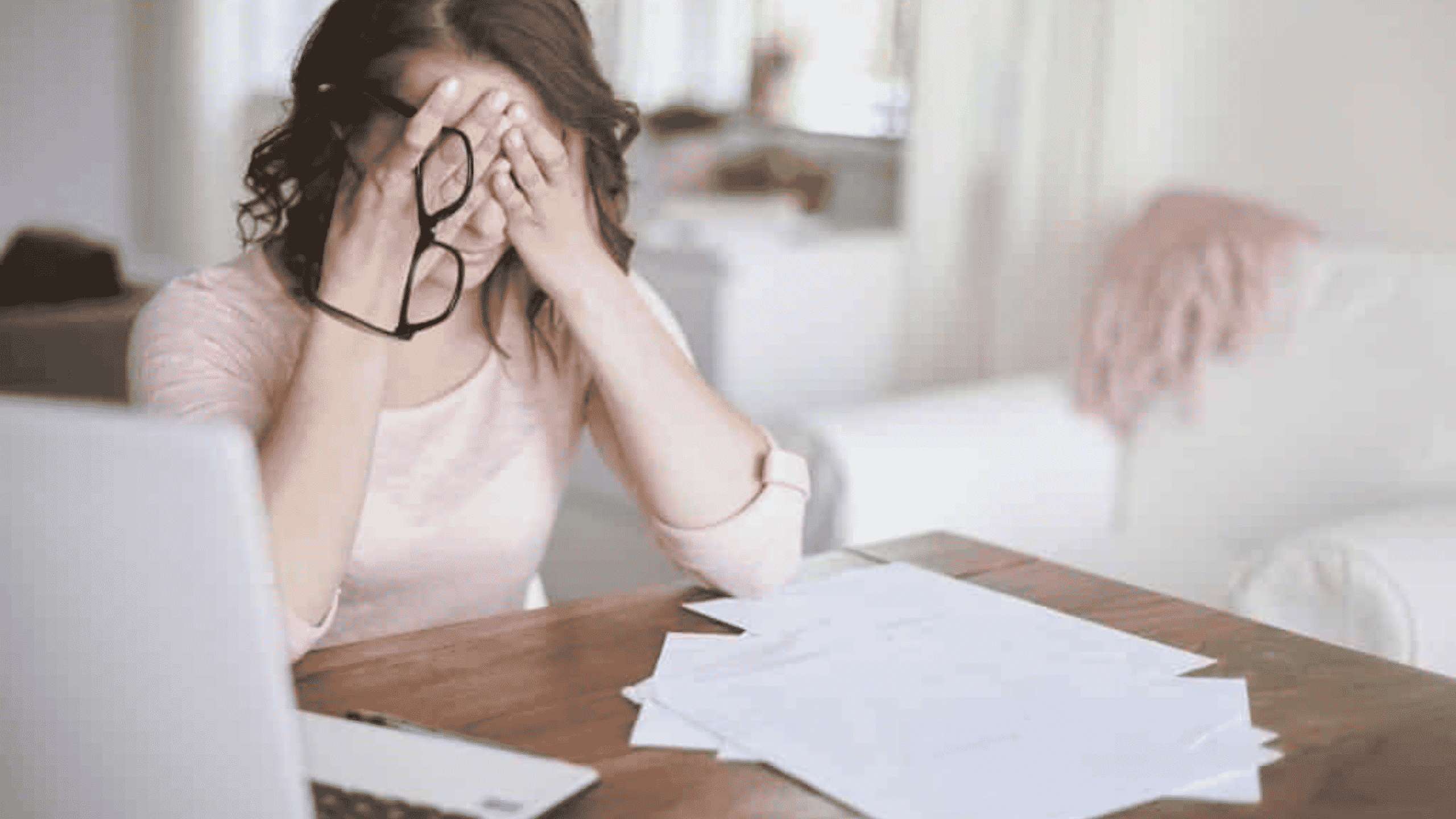 Femme épuisée se tenant la tête dans les mains devant des papiers, épuisé par un Burn-out, un Bore-out ou un Brown-out