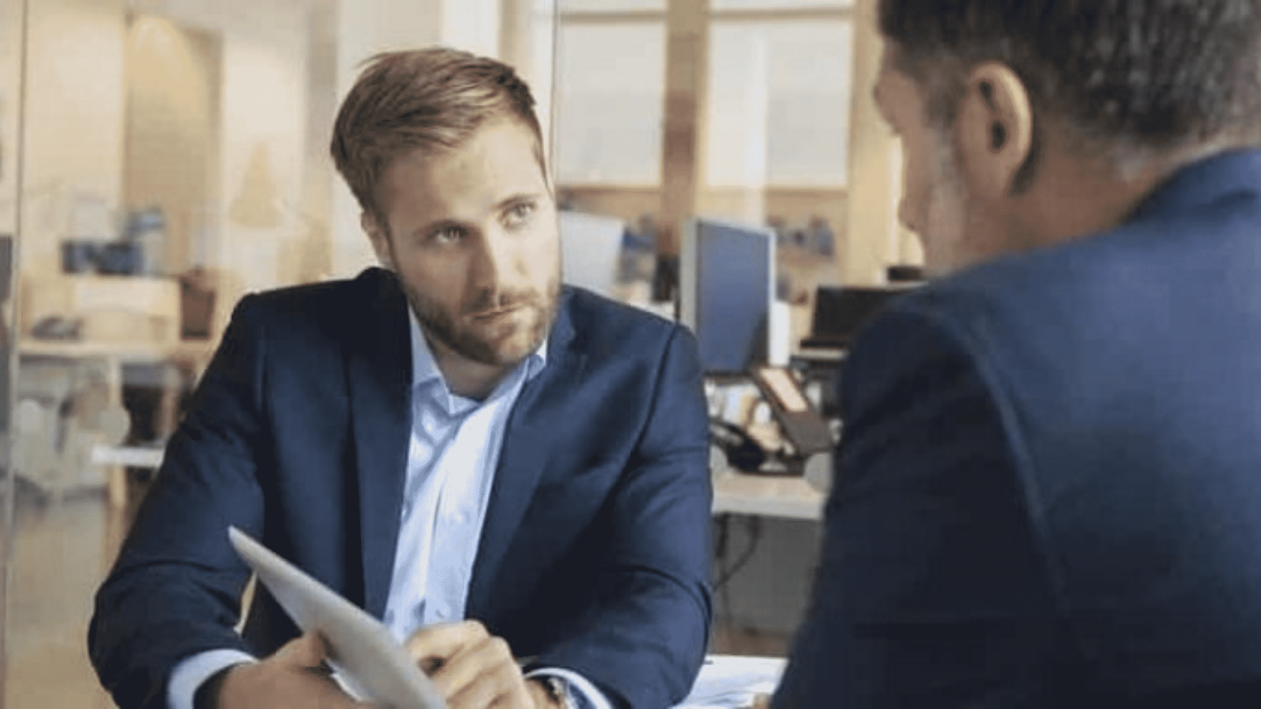 Deux hommes en entretien dont l'un qui montre un document sur un IPad.