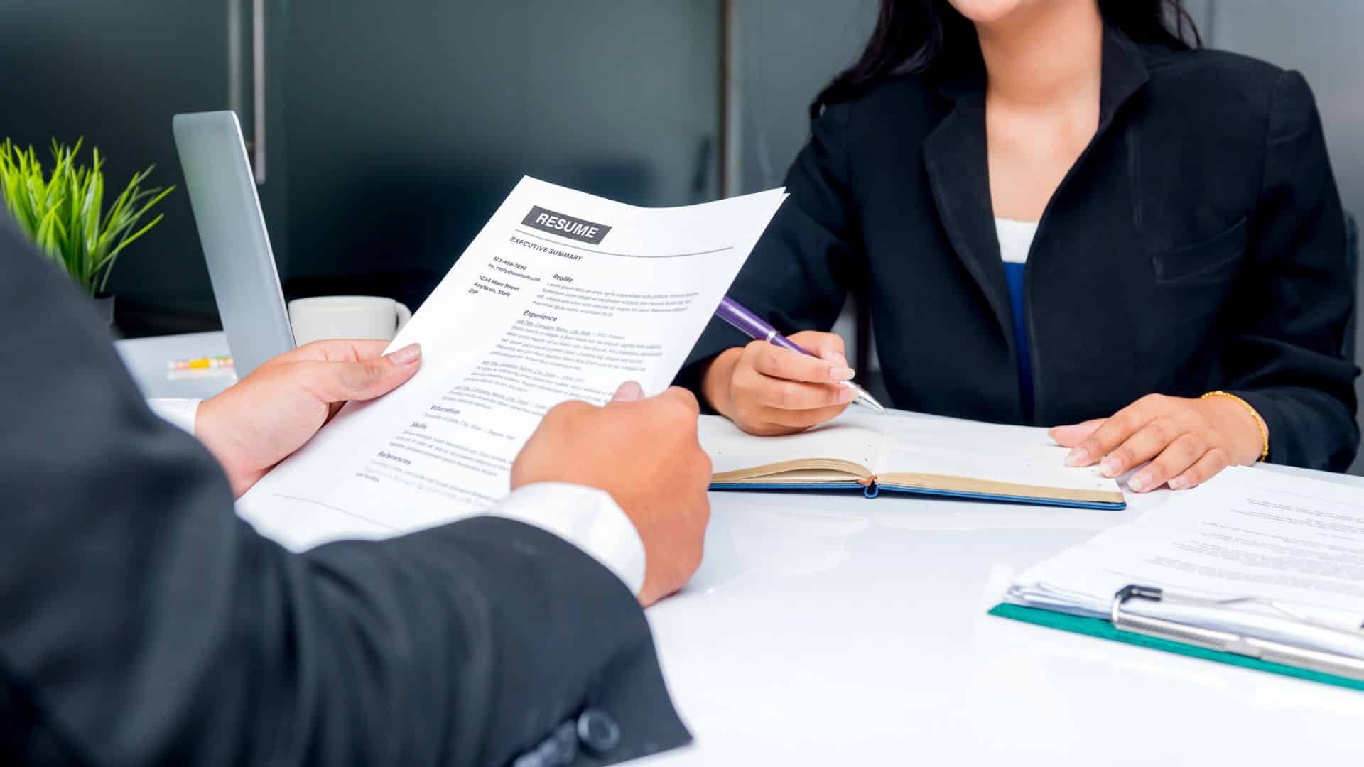 Un homme qui tien un CV avec une femme en face qui prend des notes pour illustrer le fait de savoir comment gérer les recrutements pendant les congés estivaux ?