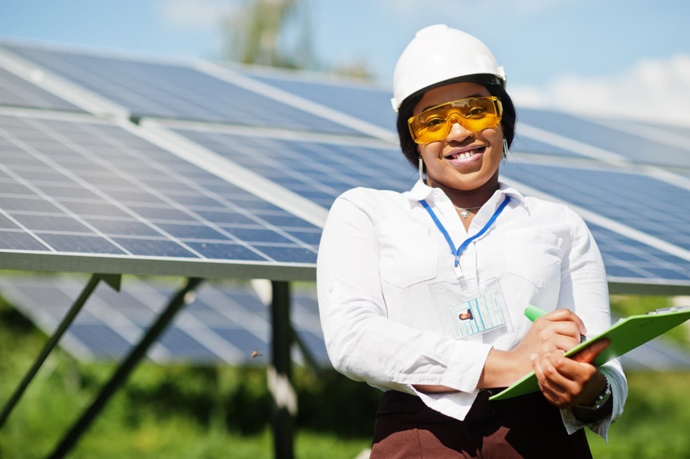Femme avec un casque de protection sur le terrain devant un panneau photovoltaïque pour illustrer la sous représentation des femmes dans les énergies renouvelables.