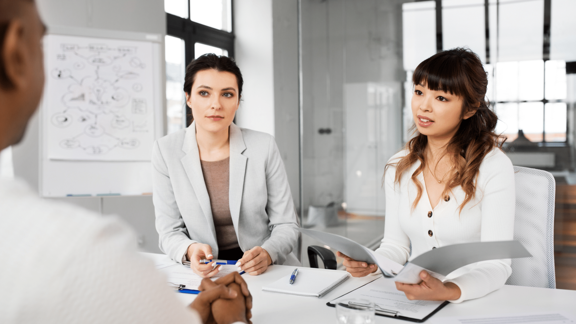 Deux femmes en face d'une autre personne de dos sur un bureau pour illustrer les questions délicates en entretien, les 5 erreurs à éviter